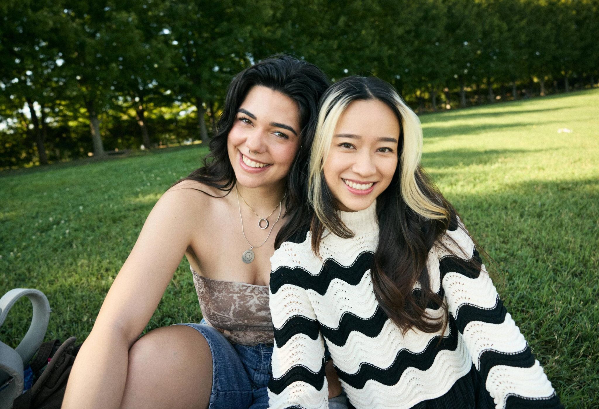 Two smiling young women sitting together on grass.